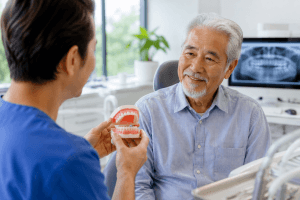 Older man speaking with a dental professional in a modern denture clinic in Toronto while reviewing denture options using a dental model in a bright and comfortable consultation setting.